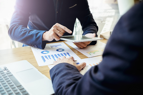 Two people viewing tablet with investment graphs on table